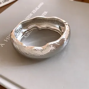 Detailed view of silver-finish wavy textured metal oval bangle on a neutral prop