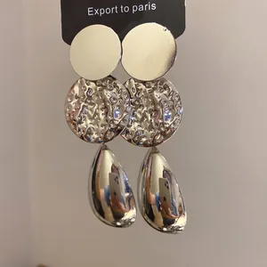 Dettaglio di orecchini color argento con trama martellata e pendente a goccia lucido.