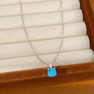 Detailopname van een minimalistische zilveren ketting met een blauwe ronde zirkoon hanger.