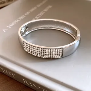 Detailed close-up of a silver pavé crystal oval bangle on a grey book background.