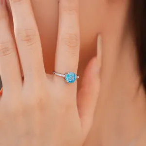 Detailopname van een zilveren ring met een ronde blauwe steen op de vinger van een model.