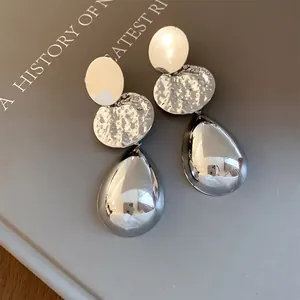 Dettaglio di orecchini color argento con disco stropicciato e lucente ciondolo a goccia