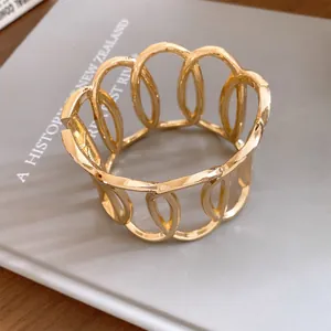Detailed macro view of a gold-tone metal open cuff bracelet with oval cut-out design.