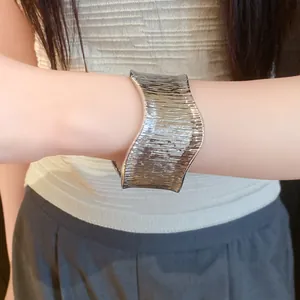 Close-up view of a textured metallic wide cuff bracelet featuring irregular wavy edges