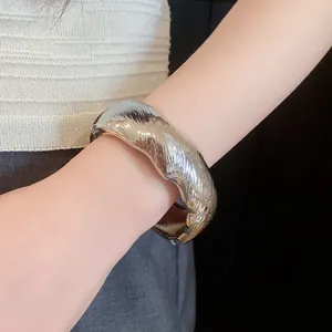 Close-up detail of a chunky silver textured oval cuff bangle worn on a female wrist