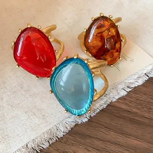 Nahaufnahme von großen Harzringen in Rot, Blau und Bernstein mit goldfarbenem Metallfinish.