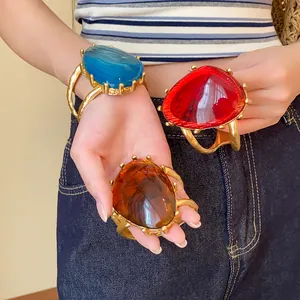 Nahaufnahme von drei auffälligen Metall-Harz-Armbändern in Blau, Rot und Bernstein