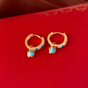 Détail de boucles d'oreilles créoles dorées avec coeurs bleus sur un coffret à bijoux rouge