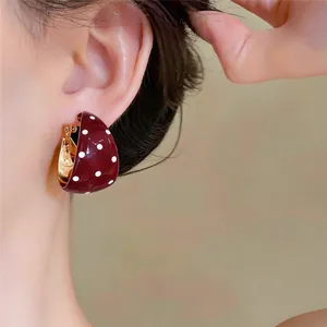 Detailed close-up shot of a retro burgundy enamel hoop earring featuring white polka dots