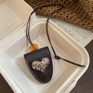 Detailaufnahme eines Anhängers mit Leopardenherz auf dunkelbraunem Brillenhalter aus Leder.