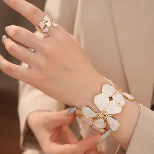 Elegante goudkleurige armband en ring set met witte emaille bloemen, detailopname.