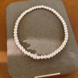 Detailopname van een witte parelarmband met een glinsterende zirkonia kraal.