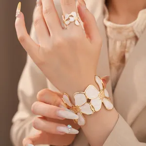 Detailopname van elegante witte emaille bloemenring en armbandset aan de hand.