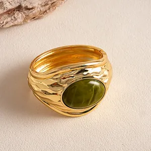Dettaglio macro di un bracciale vintage dorato con trama a pieghe e pietra di resina verde.