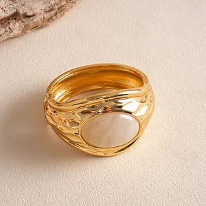 Dettaglio di un bracciale rigido in metallo dorato plissettato con intarsio in resina crema.