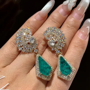 Détail de boucles d'oreilles pendantes dorées avec pierres vertes en goutte et zircons