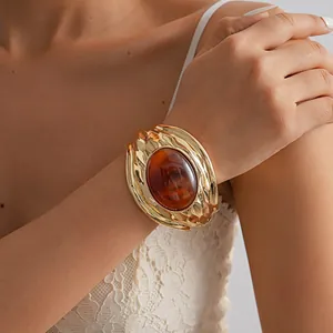 Dettaglio di un bracciale rigido vintage in metallo dorato con un grande ovale in resina.