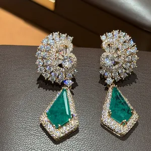 Vue rapprochée de boucles d'oreilles dorées 18 carats avec pierres vertes et zircons.