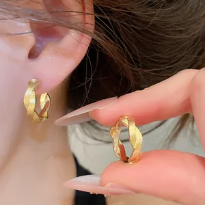 Nahaufnahme von goldfarbenen, gedrehten Metall-Creolen mit strukturierter Oberfläche am Ohr.
