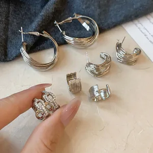 Détail de boucles d'oreilles en C argentées torsadées et d'une bague étincelante