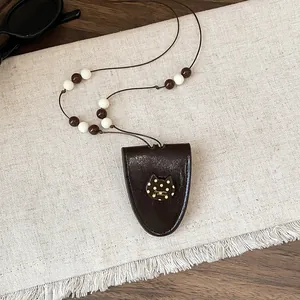 Detailopname van bruine lederen buidelketting met gestippelde kattenhanger en kralen