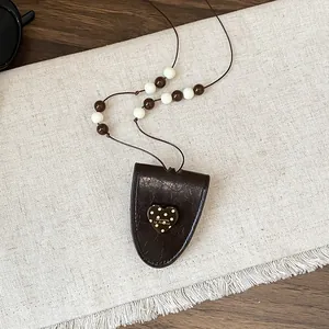 Detail van vintage leren brillenhouder ketting met hartjeshanger en kralen koord.