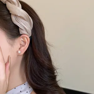Gros plan d'un serre-tête en tissu beige torsadé avec une texture plissée scintillante.