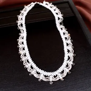 Detail van een handgemaakte witte kralenketting met glazen druppels op een zwart display