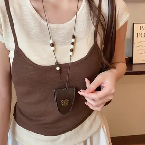 Detail van vintage leren hartjesketting gedragen bij een neutrale gelaagde outfit