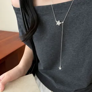 Detail shot of a minimalist silver flower pendant necklace worn on a dark grey top.