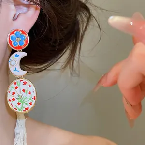 Close-up van vintage asymmetrische emaille oorbellen met bloemen- en maanpatronen op oor