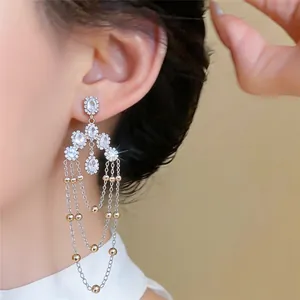 Detalle de pendientes de borla plateados con circonitas brillantes y bolas de oro