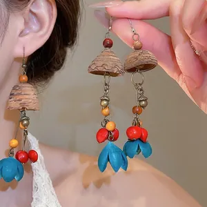 Boucles d'oreilles ethniques en bois avec glands de plantes colorés portées par un mannequin