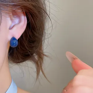 Nahaufnahme minimalistischer blauer Teardrop-Ohrstecker am Ohr eines Modells