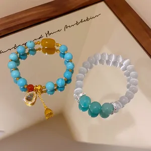 Close-up of turquoise and cat's eye beaded bracelets with a gold gourd charm on a mirror.