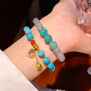 Close-up detail of turquoise and resin beaded bracelets with a gold gourd pendant charm