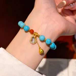 Close-up view of a turquoise beaded bracelet featuring a sparkling gourd charm on a wrist