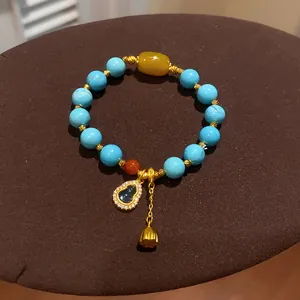 Close-up detail of turquoise resin beaded bracelet featuring gold hulu and lotus bud pendants