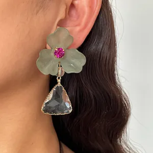 Gros plan d'une boucle d'oreille fleur en acrylique avec pendentif triangle gris.
