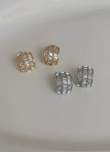 Hochwertiges Detail von minimalistischen Gold- und Silber-Halbbogenohrringen mit Zirkon.