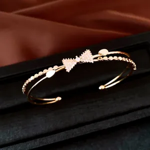 Detailansicht eines goldenen zweilagigen Armreifs mit funkelndem Zirkon-Schleifenmotiv.