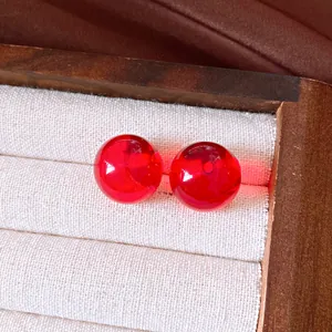 Makro-Detail von lichtdurchlässigen hellroten Kugelohrsteckern in einem Holzschmuckfach