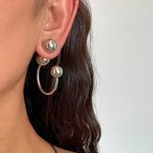 Détail de boucles d'oreilles créoles géométriques en C argentées avec boules en métal poli