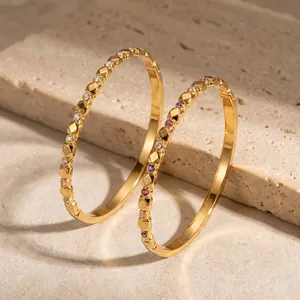 Close-up of gold-plated geometric bangles with colorful zircon insets on stone surface