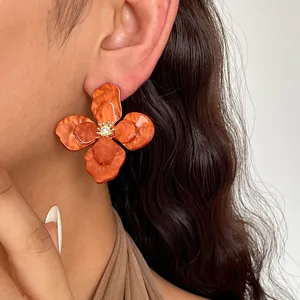Primo piano di orecchini a fiore in acrilico arancione con trama marmorizzata e strass centrale
