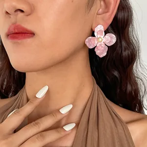 Dettaglio dell'orecchino a fiore in acrilico rosa marmorizzato con strass indossato da modella