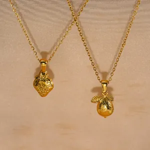 Détail des pendentifs en forme de fraise et citron en acier inoxydable doré.