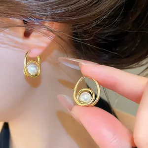 Close-up of vintage pearl hoop earring with gold drop design on model ear and hand