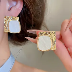 Dettaglio di orecchini quadrati dorati con elegante inserto in madreperla bianca.