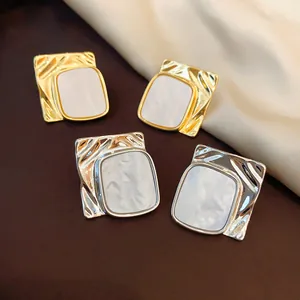 Dettaglio macro di orecchini quadrati oro e argento con trama metallica increspata.